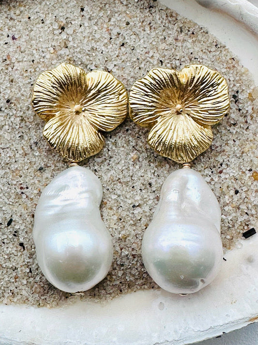 JMNYC Designs Large Baroque Pearl Earrings feature 1.5" vermeil "Hibiscus" post tops, each showcasing an irregular baroque pearl drop displayed on a bed of sand.