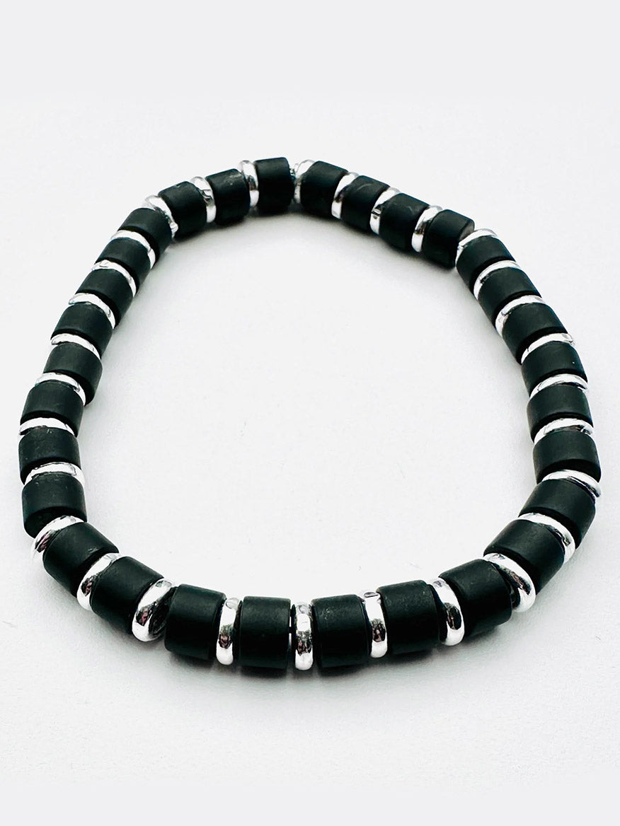 Introducing the JMNYC Designs Matte Black Onyx and Sterling Silver Rondelle Stretch Bracelet—a Limited Edition piece featuring alternating matte black onyx cylindrical beads and sterling silver rondelle spacers, beautifully arranged in a circle against a white background.