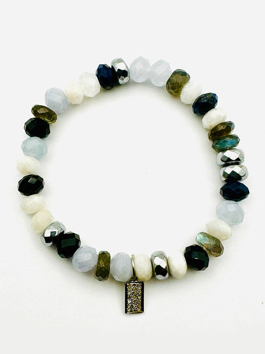 The JMNYC Designs stretch bracelet features moonstone, lapis, labradorite, black spinel, and pyrite beads with a sterling diamond dog tag charm.