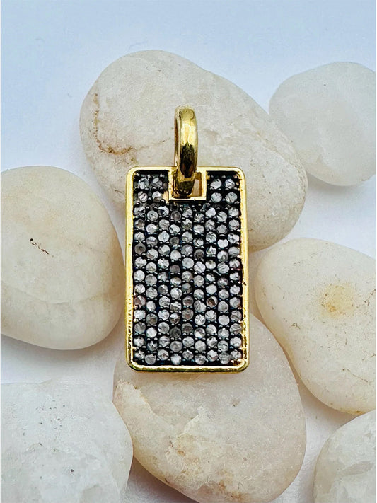 The JMNYC Designs Vermeil & Rhodium Small Pave Diamond Dog Tag Pendant features a rectangular 18K yellow gold design with a loop, adorned with numerous small round diamonds, shown on smooth white stones.