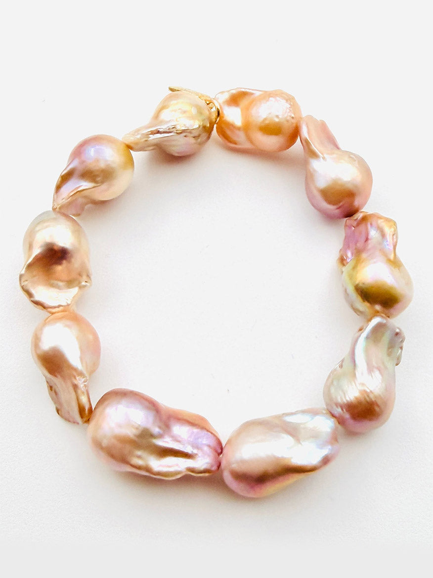 Presenting the JMNYC Designs Peach Natural Baroque Pearl Stretch Bracelet, measuring 7.5", crafted with large, irregularly shaped peach-hued baroque pearls and featuring elegant gold vermeil accents including a diamond dogtag, beautifully arranged in a circle on a white background.