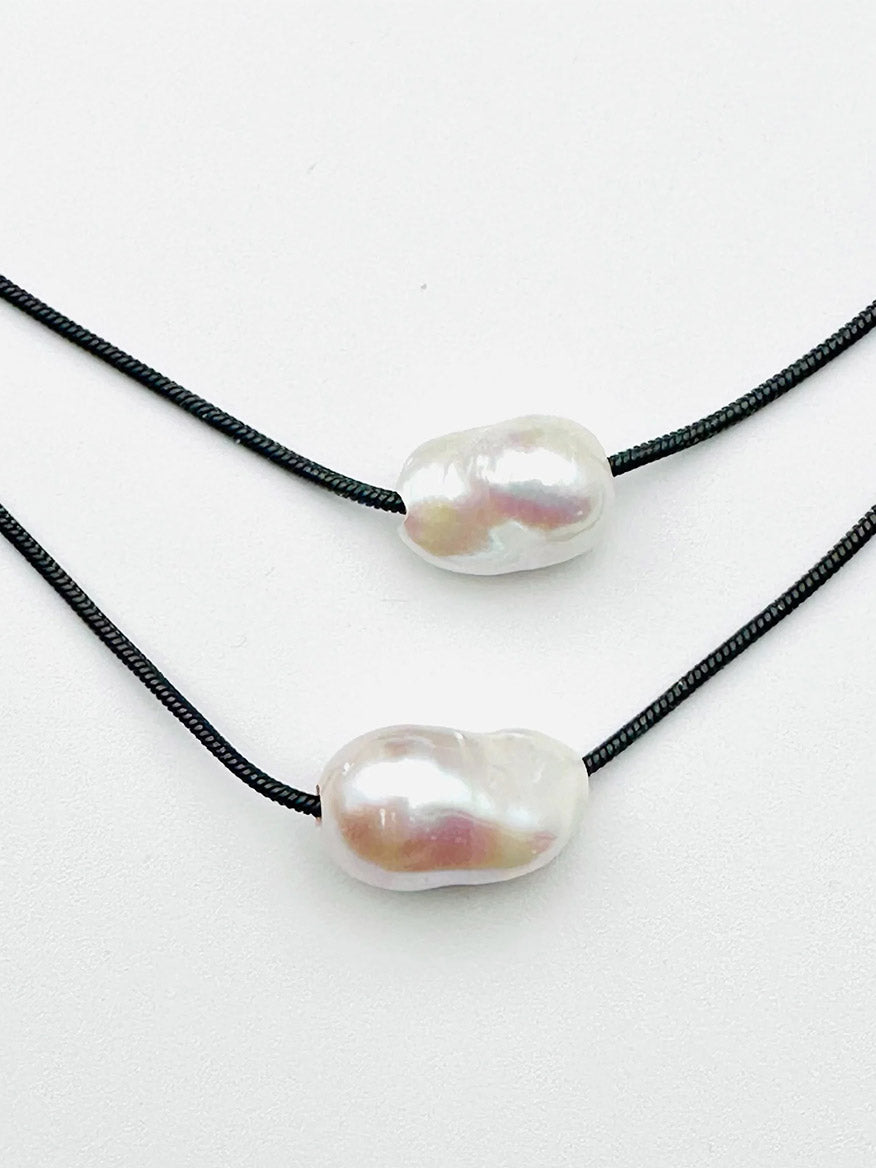 The JMNYC Designs Removable Baroque Freshwater Pearl Black Rhodium Snake Chain features two irregularly shaped baroque freshwater pearls threaded onto separate black rhodium snake chains, displayed on a plain white background.