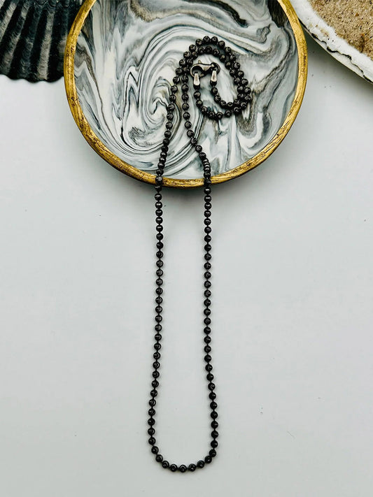 The JMNYC Designs Sterling Silver Rhodium Finish Ball Chain Necklace 18" is neatly arranged on a round marbled dish with a gold rim, placed on a white surface.