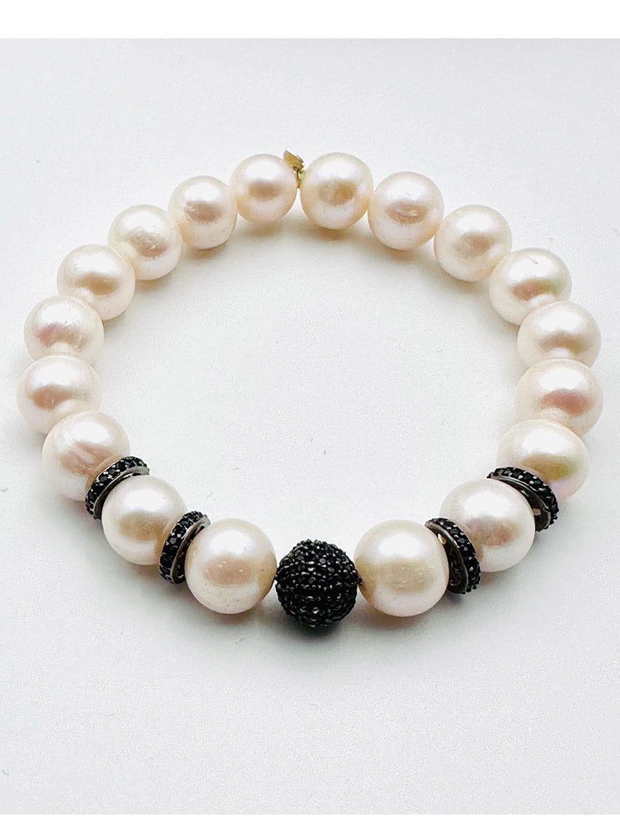The JMNYC Designs Round White Freshwater Pearl Bracelet with Black Spinel & Rondelles features large, round white pearls accented by small black spinel rondelles as spacers and a single, larger black bead centerpiece, displayed on a plain white background.