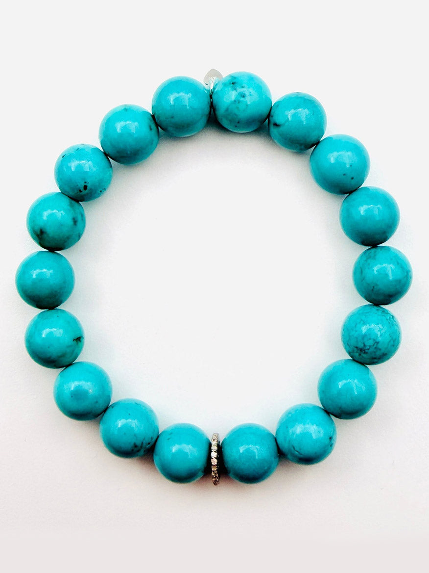 The JMNYC Designs Turquoise Smooth Ball Bracelet with Sterling Silver Diamond Rondelle, 7.25", features round turquoise beads and a sterling silver spacer bead, arranged in a circle on a plain white background.