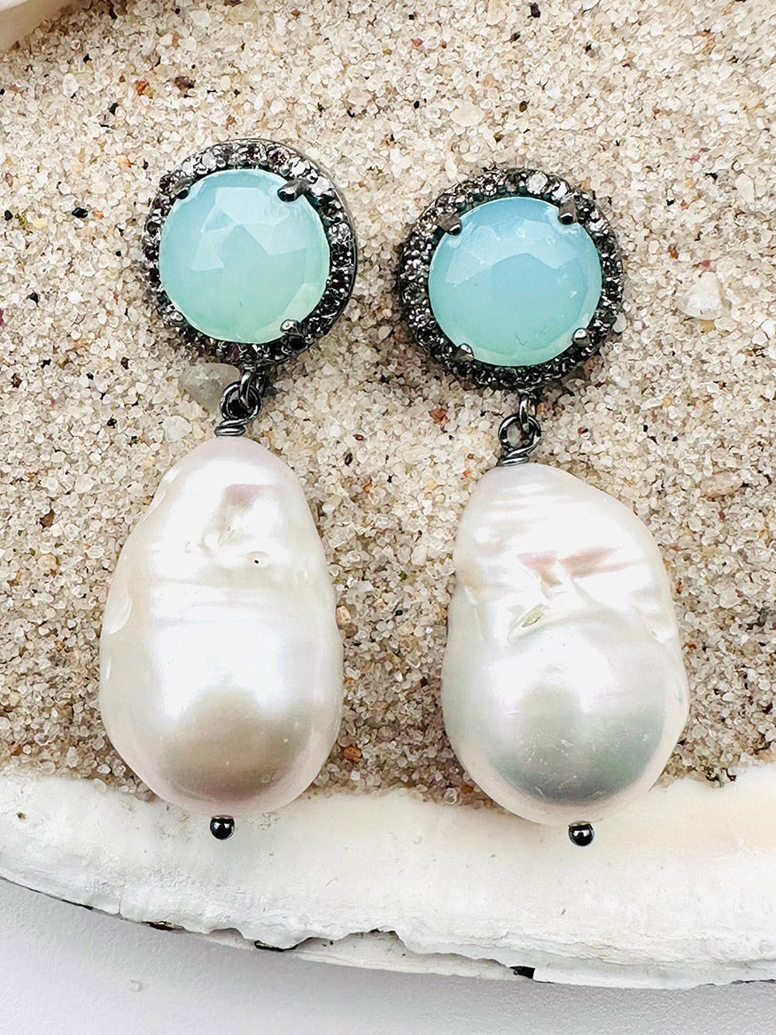 A pair of exquisite JMNYC Designs White Baroque Pearl, Peru Chalcedony & Diamond Earrings featuring luminous baroque pearls and round faceted light blue Peru chalcedony stones, elegantly displayed on a sandy surface.