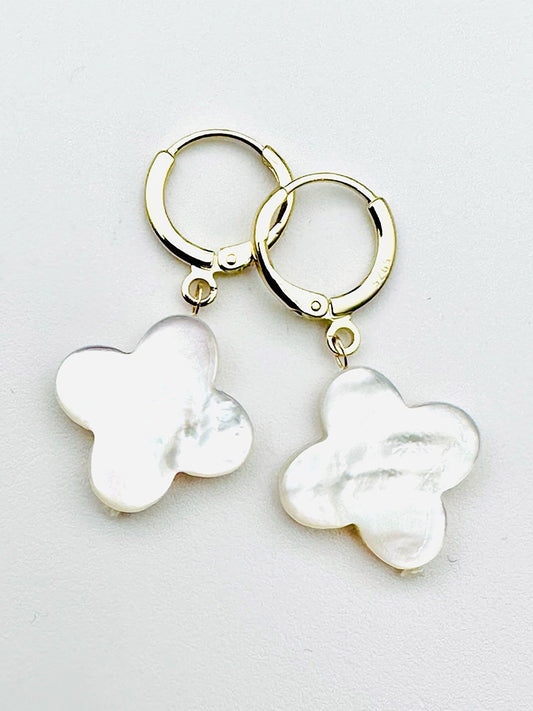 JMNYC Designs White Mother of Pearl Clover Gold Fill Huggie Earrings feature gold fill hoops with dangling, irregularly shaped white mother of pearl charms in a four-petal clover design, shown against a plain white background.