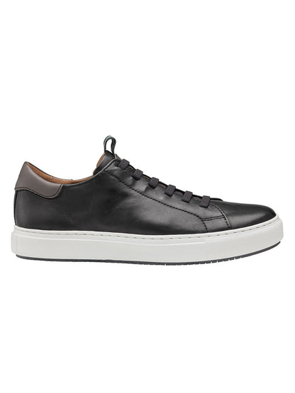 The J & M Collection Anson Lace-to-Toe in Black Sheepskin is a black leather sneaker with a white rubber sole, black laces, and a brown accent at the heel, featuring modern cushioning for enhanced comfort.