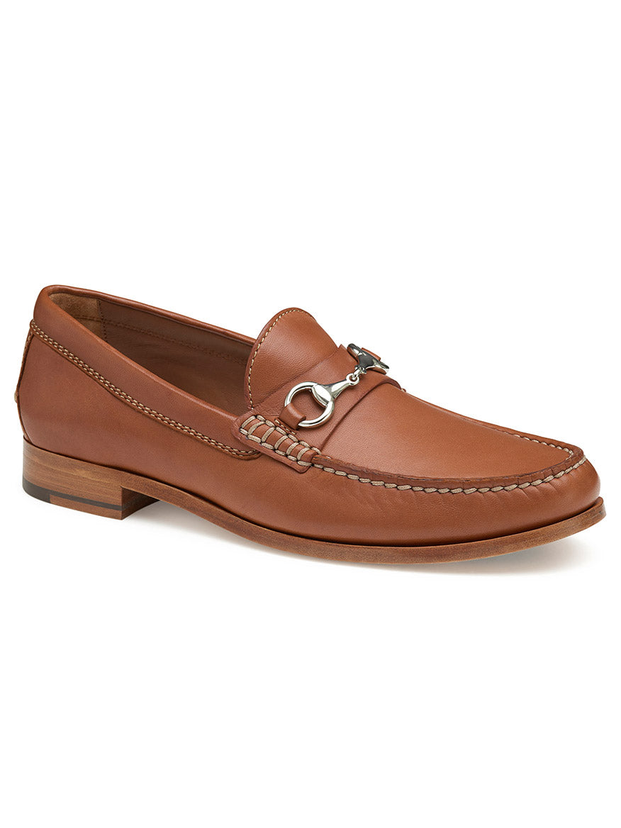 The J & M Collection Baldwin Bit in Cognac Sheepskin is a brown leather loafer adorned with a metal bit decoration on the front, detailed stitching, and a wooden heel, all crafted from sheepskin leather.