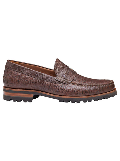 The J & M Collection Baldwin Lug Penny in Mahogany Scotch Grain is a brown loafer with a textured leather surface and rugged rubber sole, shown in profile, featuring a cushioned footbed for added comfort.