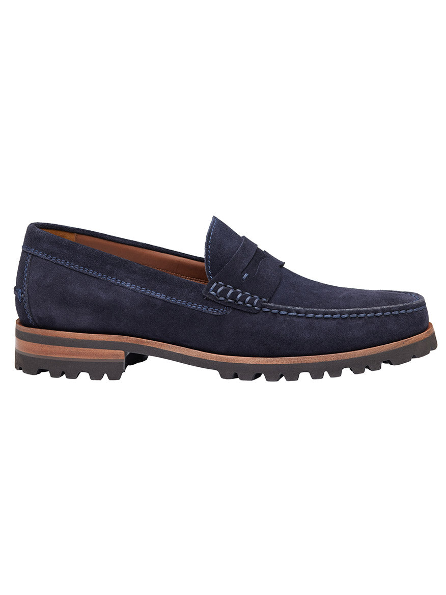 The J & M Collection Baldwin Lug Penny in Navy English Suede is a dark blue suede penny loafer with a brown sole, moccasin construction, detailed stitching, and leather lining, shown from the side.