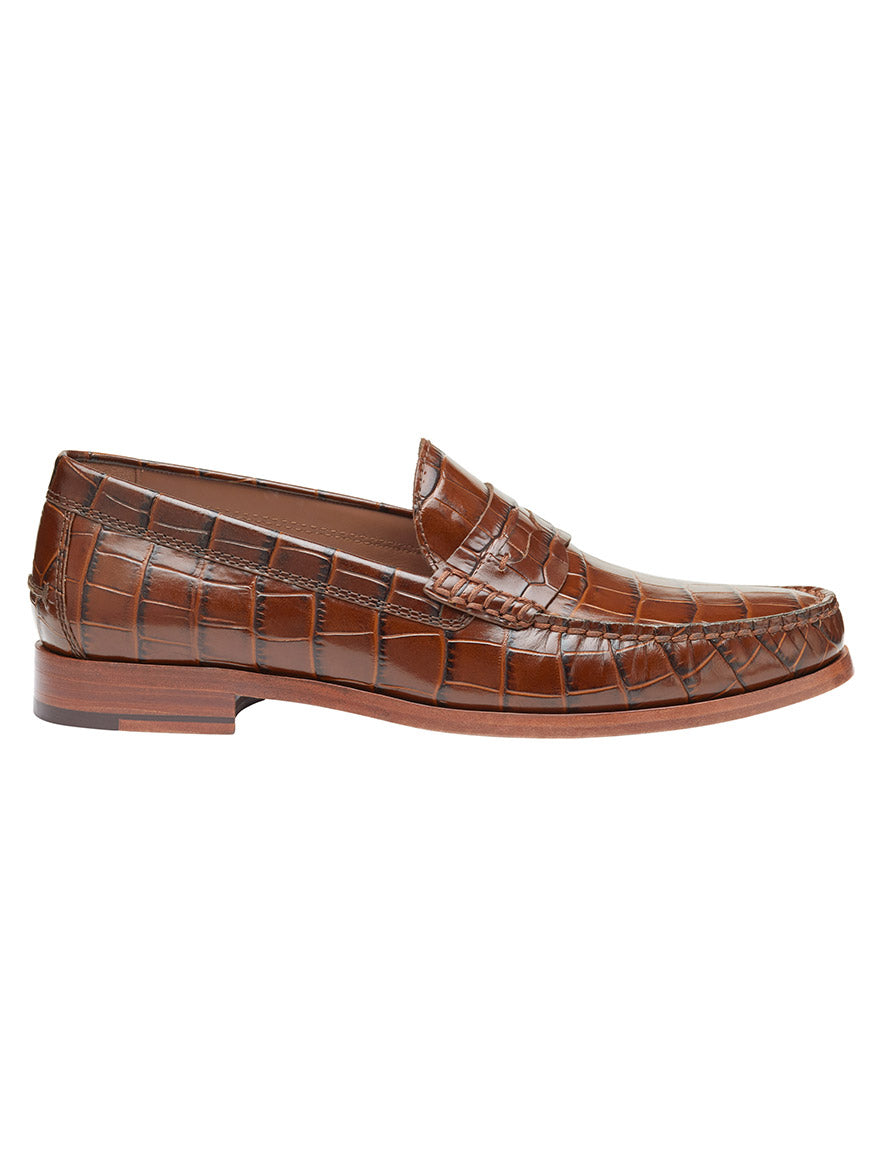 The J & M Collection Baldwin Penny in Mahogany Croc Print Calfskin is a brown leather loafer featuring an Italian calfskin upper with a crocodile pattern and a low wooden heel.