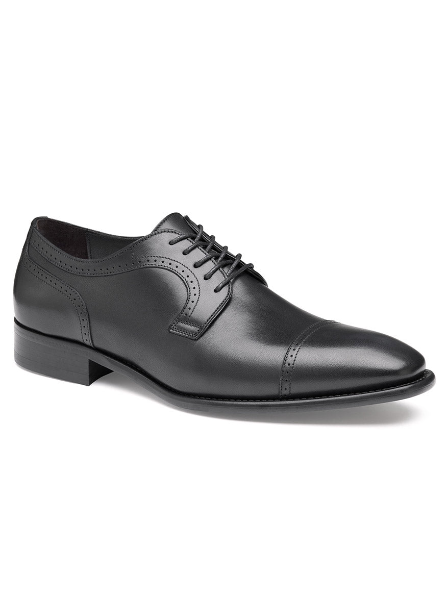 Displayed against a white background is the J & M Collection Cormac Cap Toe in Black Italian Calfskin from Johnston & Murphy. This black leather oxford shoe features a cap toe design, laces, and a slight heel. It includes a comfortable leather footbed and a rubber injection forepart for added durability.