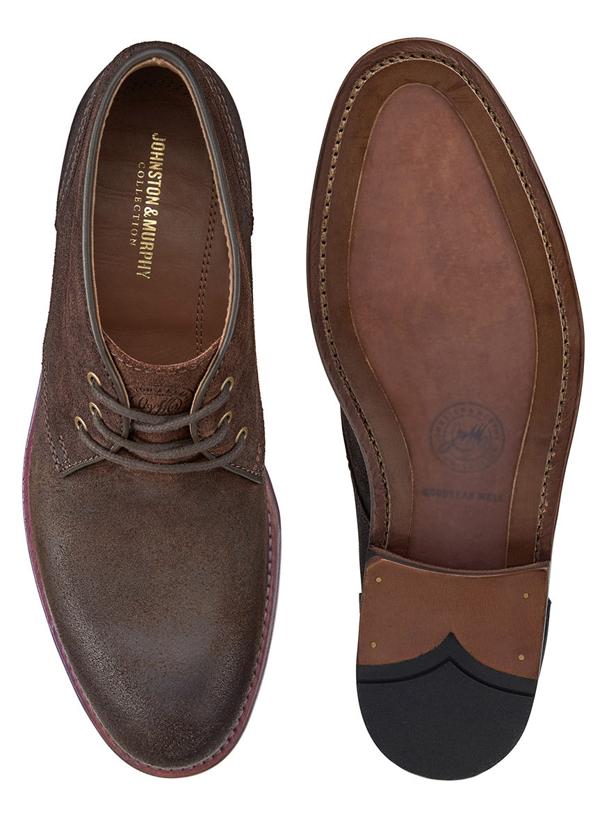 A pair of J & M Collection Dudley Chukka in Brown Waxed English Suede, showcased from both the top and bottom. The left shoe displays the brand name "Johnston & Murphy" inside, while the right shoe reveals the sole with detailed stitching, emphasizing their Goodyear welt construction.