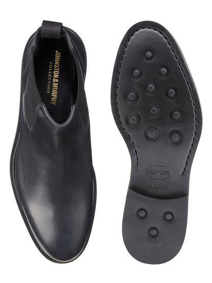 A pair of black Italian calfskin Chelsea boots from the J & M Collection Hartley; one boot is viewed from the top, revealing a leather-covered footbed, and the other displays a Vibram EVA outsole.