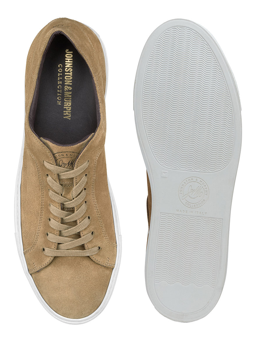 A pair of taupe J & M Collection Jared Lace-To-Toe sneakers in Italian suede with white rubber soles. One shoe is shown from the side, and the other is displayed bottom-up, highlighting the tread pattern. Featuring a cushioned footbed and leather lining, with the brand name visible on the insole.