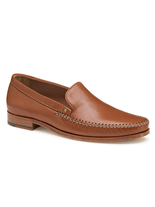 The J & M Collection Baldwin Venetian in Cognac Sheepskin is a brown leather slip-on loafer, crafted with moccasin construction and detailed stitching. It features a low heel, slightly pointed toe, and side-view cushioned footbed for enhanced comfort.