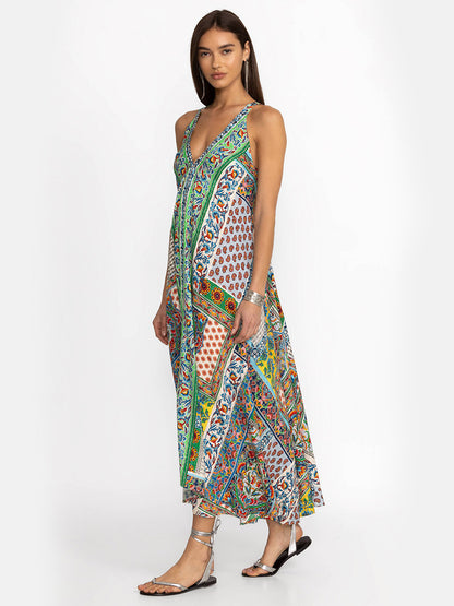 A woman modeling the Johnny Was Eva Dress in Diskana, a colorful, patterned maxi dress with one shoulder strap, standing against a plain background, paired with silver heels.