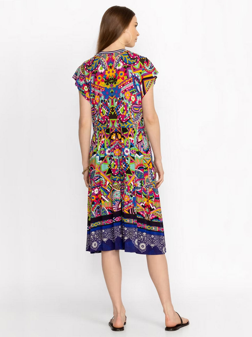 A woman in a Johnny Was Janie Favorite Tiered Tea Length Dress in Demarne Print stands facing away from the camera, showcasing the design of the back of the dress. She is on a plain white background.