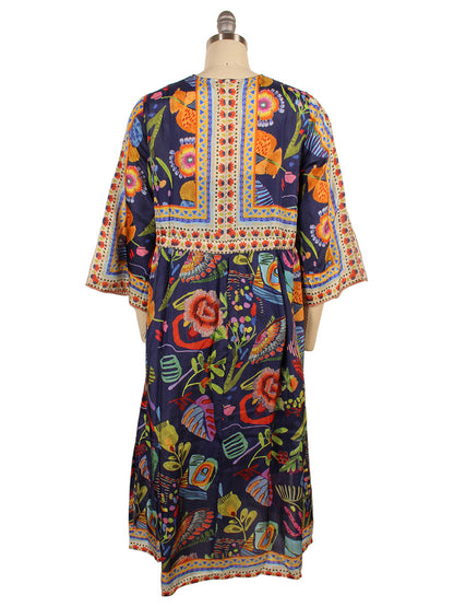 The Johnny Was Saskia Midi Dress, in a Farout Scarf Print, displayed on a mannequin, showcases vibrant floral and geometric patterns. With bright red, orange, green, and blue hues, it features elegant kimono sleeves for added sophistication.