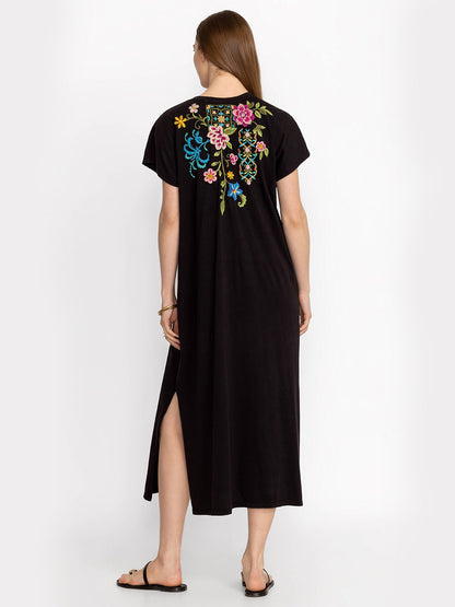 A woman in a Johnny Was Sheri Relaxed Knit Dress in Black with colorful floral placement embroidery on the back, standing in profile view, on a plain background.