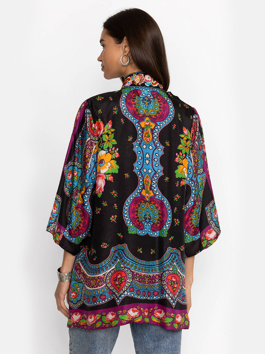 Woman modeling a vibrant, patterned silk Johnny Was Yena Reversible Kimono in Rose Spark with floral and paisley designs on a plain background. She is viewed from the back.