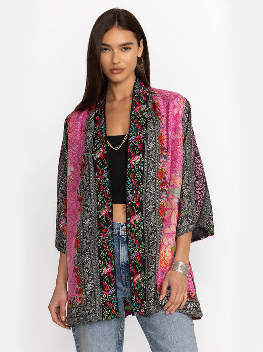 A woman models a colorful floral silk Johnny Was Yena Reversible Kimono in Rose Spark over a black top and jeans against a white background.