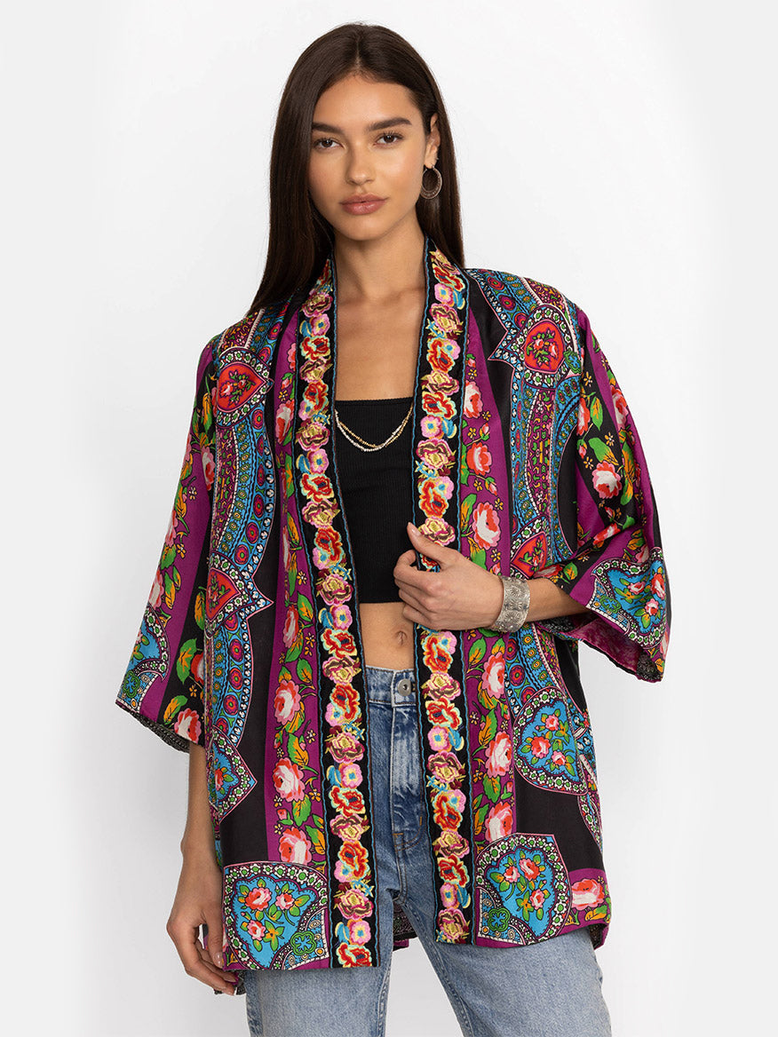 Woman in a vibrant, patterned Johnny Was Yena Reversible Kimono in Rose Spark over a black top and denim jeans, posing with one hand on her hip.