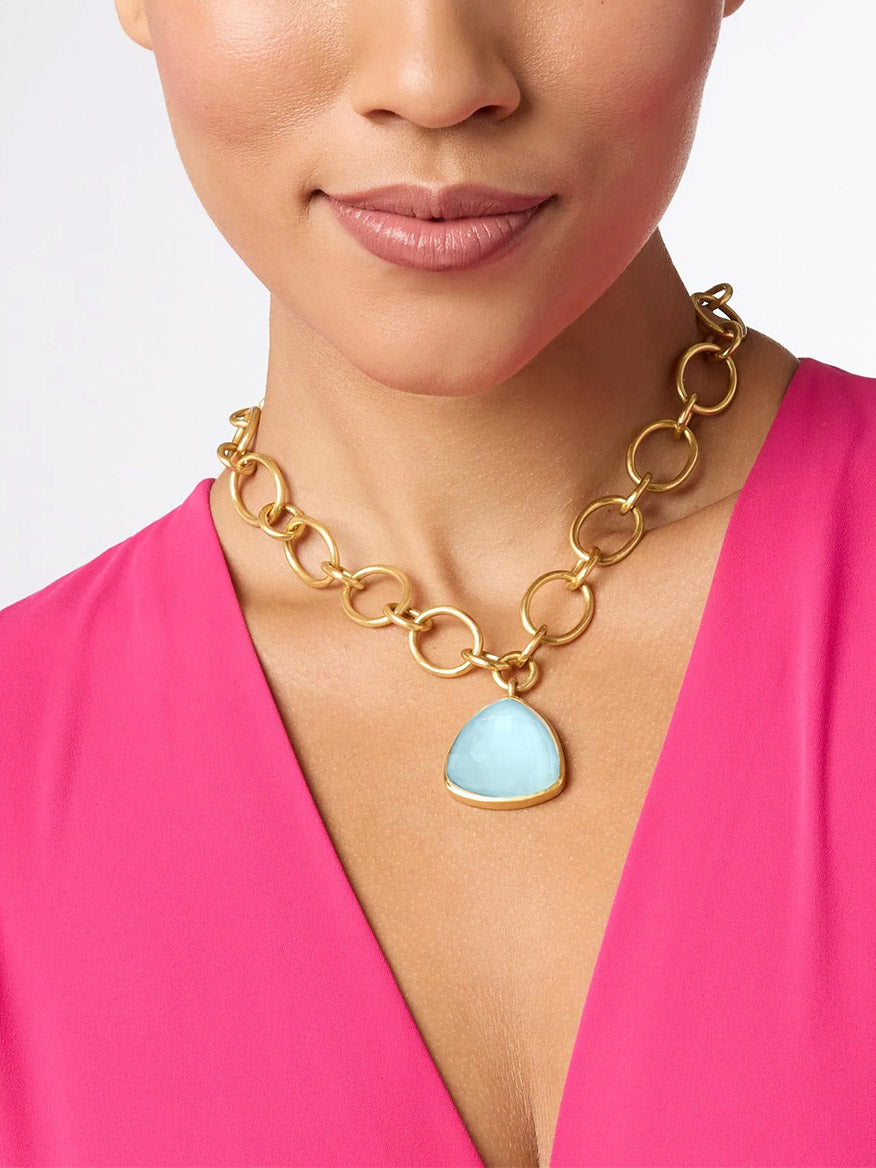 Close-up of a woman wearing a Julie Vos Aquitaine Statement Necklace in Iridescent Capri Blue with a large trillion cut gemstone pendant, dressed in a pink blouse.