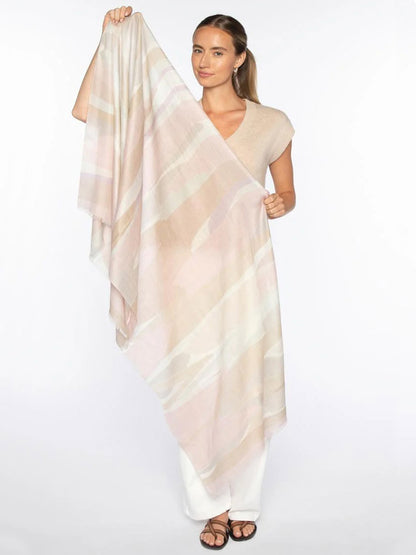 A woman holds the Kinross Abstract Landscape Print Scarf in Lilac Multi, styled with a beige top, white pants, and sandals against a white background.