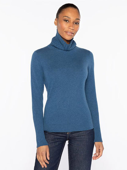 A woman stands against a plain background wearing the Kinross Chunky Trim T-Neck in Sapphire with dark jeans, her hair pulled back and arms relaxed at her sides.