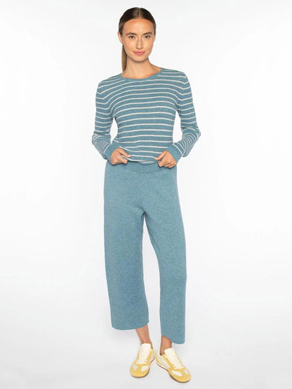 A woman stands against a white background wearing a blue and white striped long-sleeve top, Kinross Doubleknit Crop Pant in Denim, and yellow sneakers.