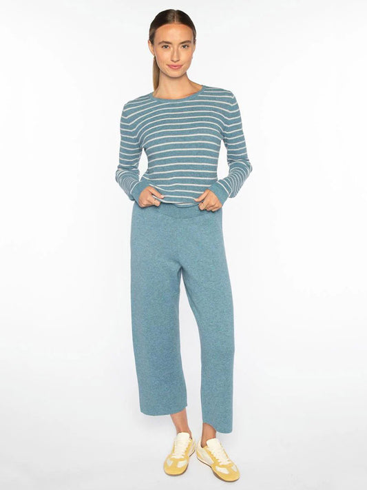 A woman stands against a white background wearing a blue and white striped long-sleeve top, Kinross Doubleknit Crop Pant in Denim, and yellow sneakers.