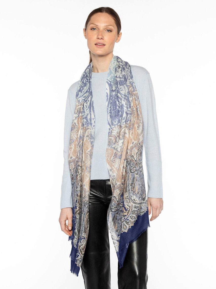 A person wearing a light blue top, black pants, and a long Kinross Faded Paisley Print Scarf in Navy Multi.