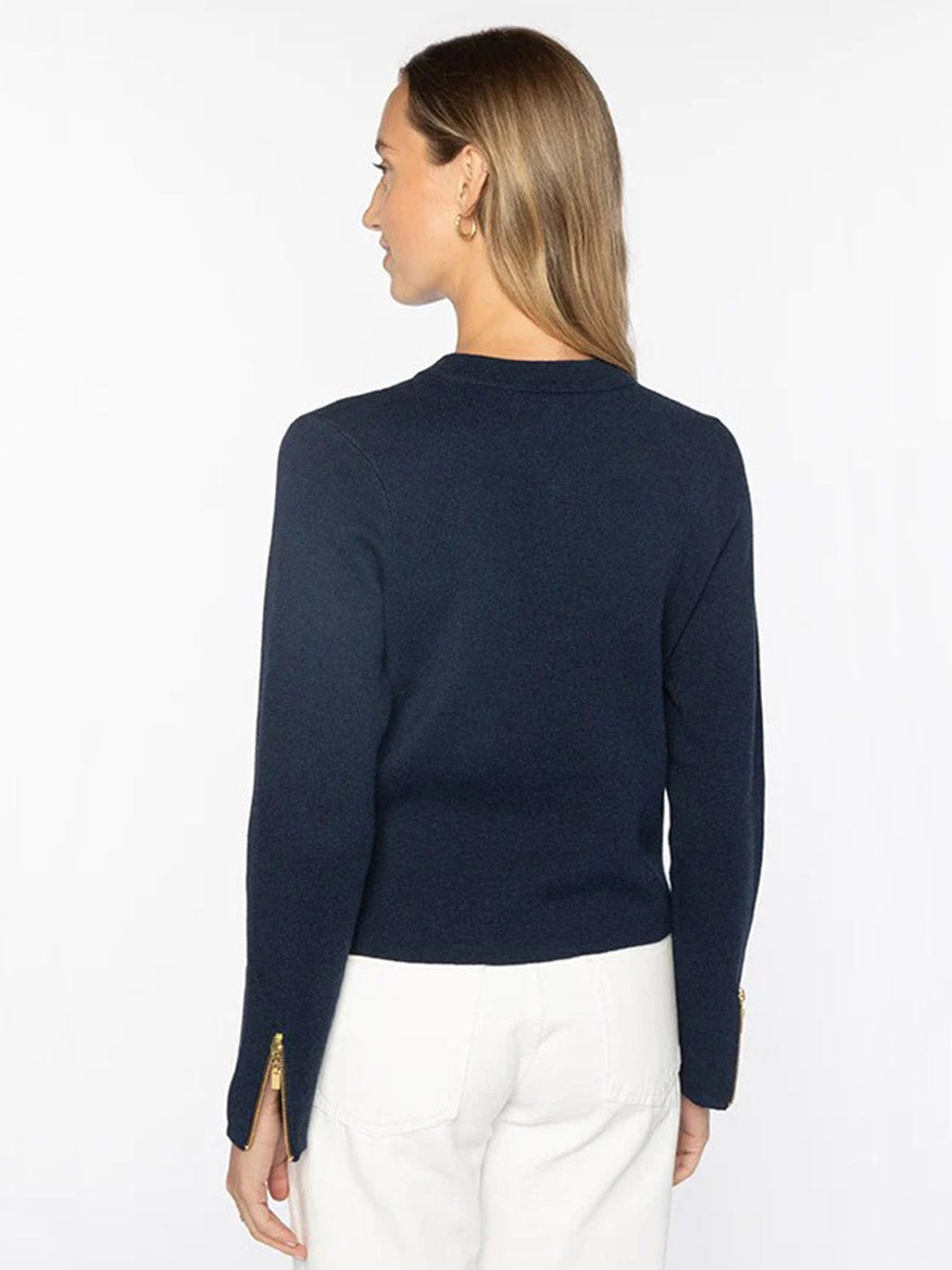 Woman stands with her back to the camera, wearing a Kinross Fitted Zip Cardigan in Navy and white pants against a plain white background.