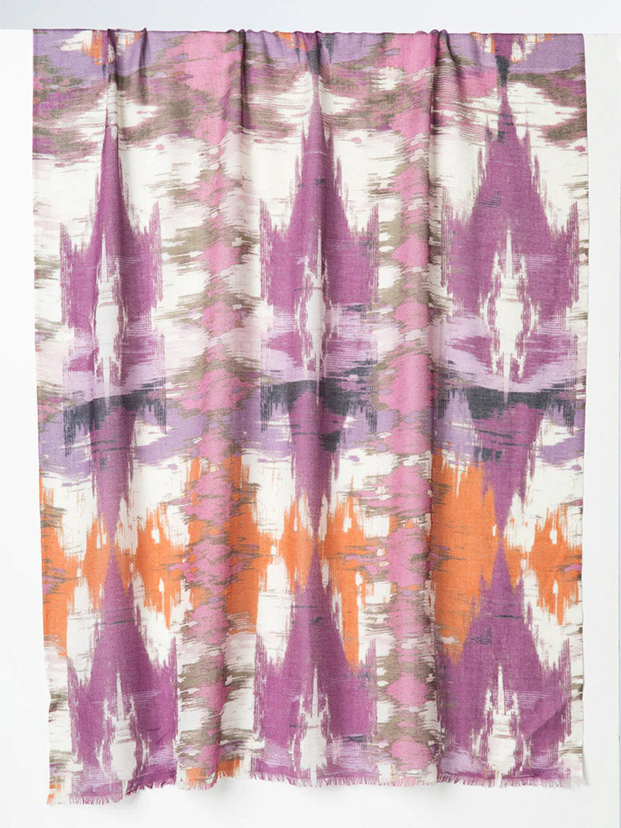 A stylish addition to any space, the Kinross Natural Ikat Print Scarf in Black Cherry Multi showcases an abstract ikat-inspired pattern in hues of purple, orange, and gray on a white backdrop.