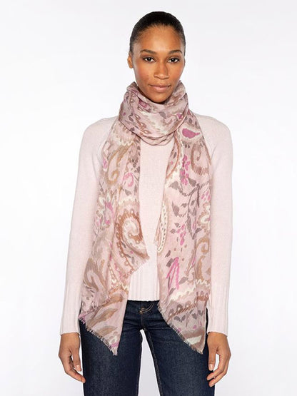 A woman in a light pink long-sleeve sweater, dark jeans, and the Kinross Painted Paisley Print Scarf in Oat Multi stands against a plain white background.