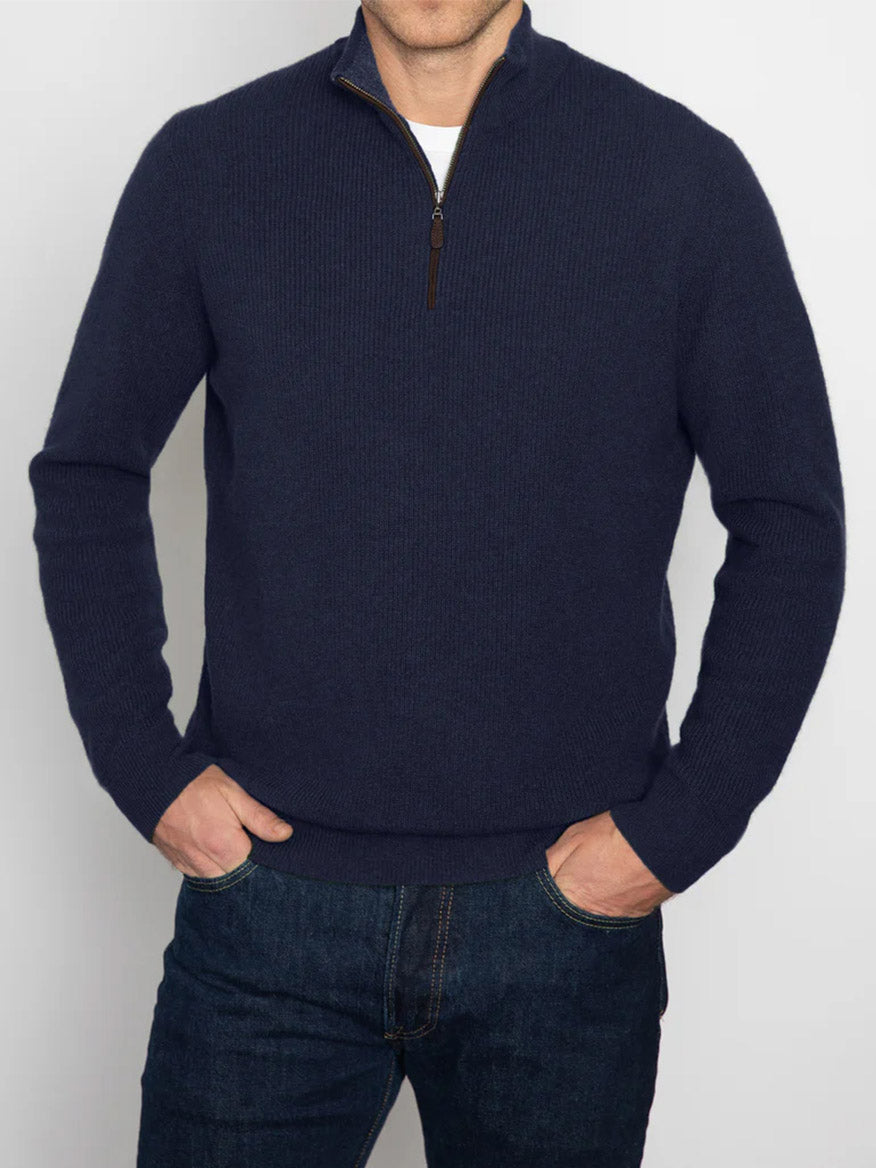 A person exudes a sophisticated look, wearing the Kinross Suede Trim Rib Quarter Zip Mock Sweater in Navy/Flannel paired with blue jeans, standing with hands in pockets.