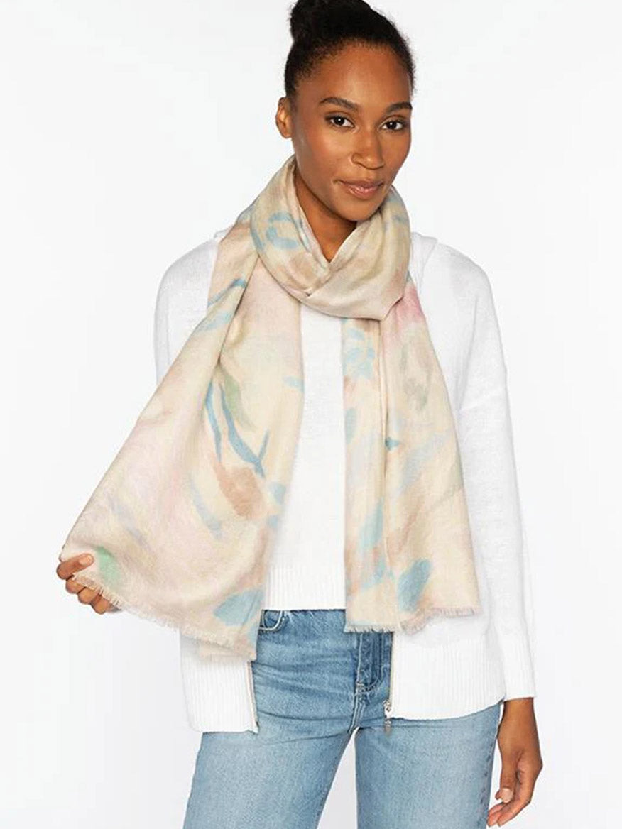 A woman wearing the Kinross Soft Floral Print Scarf in Pebble Multi draped over a white sweater and blue jeans, standing against a plain white background.