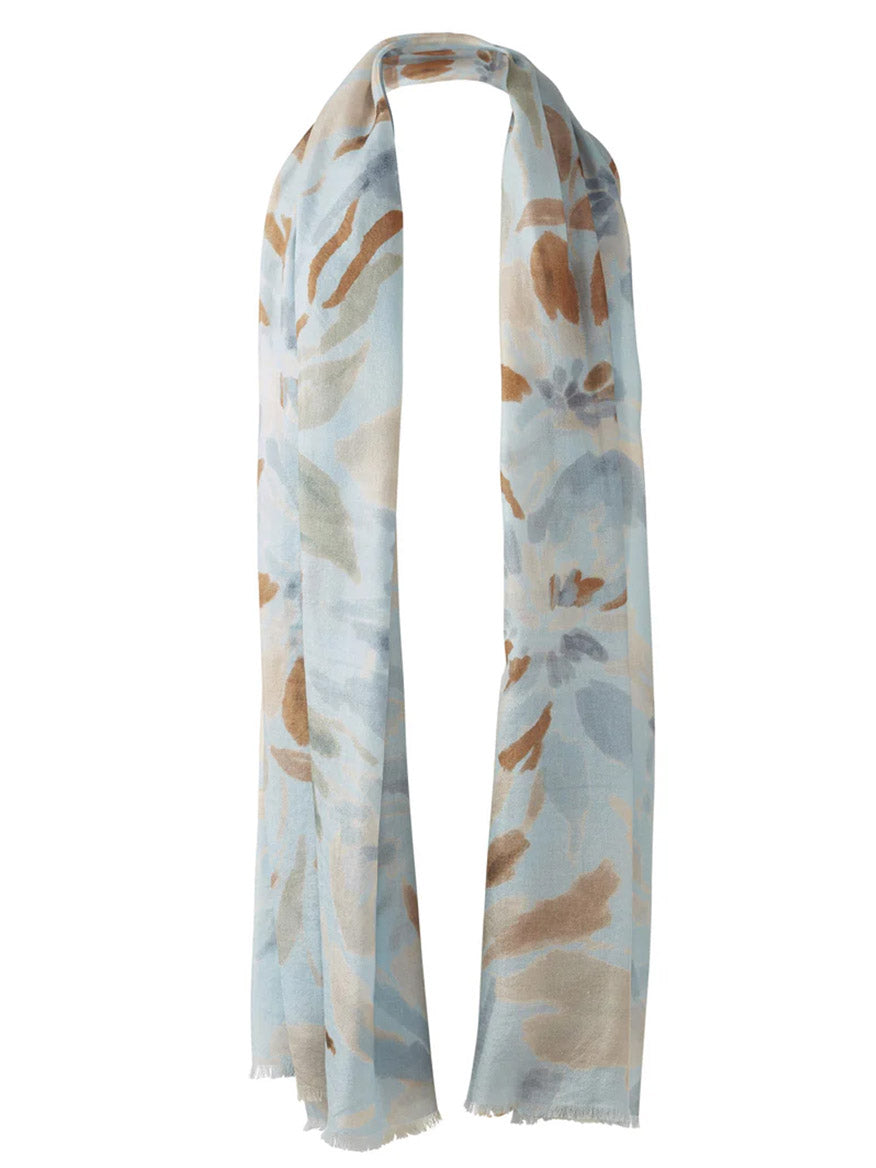 The Kinross Soft Floral Print Scarf in Skyway Multi features a light blue, brown, and beige floral pattern on soft fabric with fringed edges, shown hanging with both ends draped down.