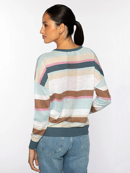 Woman with dark hair in a low ponytail wearing the Kinross Multi-Color Stripe Vee in Multi and blue jeans, standing with her back turned and glancing to the side against a plain background.