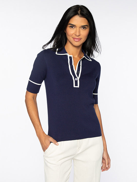 A woman with dark hair wearing a Kinross Tipped Button Polo in Navy with elbow-length short sleeves and white trim stands with one hand in her pocket and smiles at the camera.