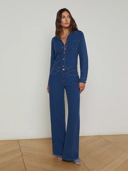 A woman stands indoors in a high-rise, wearing a long-sleeved chambray shirt and L'Agence Alicent Wide-Leg Jean in Heron, paired with open-toe heels.