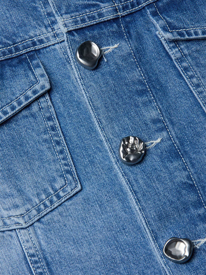 Close-up of the L'Agence Anouk Jean Jacket in Grant, a collarless blue indigo denim piece with silver irregular metal buttons and visible stitching by the chest pocket.
