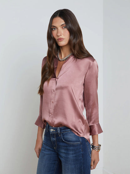 A person with long dark hair is wearing the L'Agence Dani Blouse in Mauve Rose and jeans, posing against a white background.