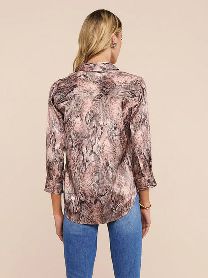 A woman with blonde hair seen from the back, wearing the L'Agence Dani Blouse in Mauve Multi Western Snake Print and blue jeans against a beige background.
