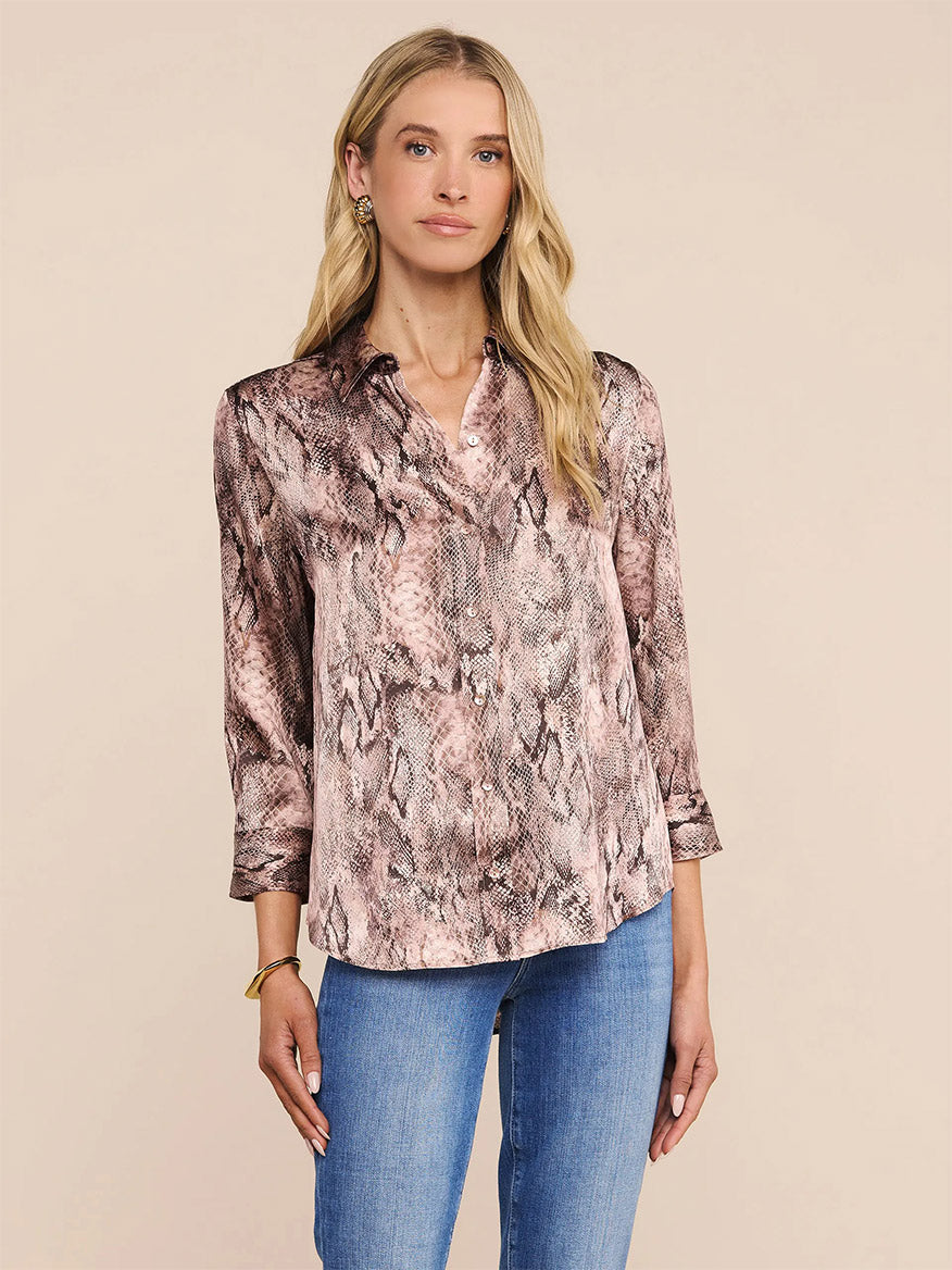 Woman wearing the L'Agence Dani Blouse in Mauve Multi Western Snake Print with blue jeans, standing against a plain beige background.
