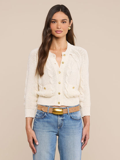 A woman wears the L'Agence Darcy Cable Knit Cardigan in Ivory paired with blue jeans, standing against a plain beige background.