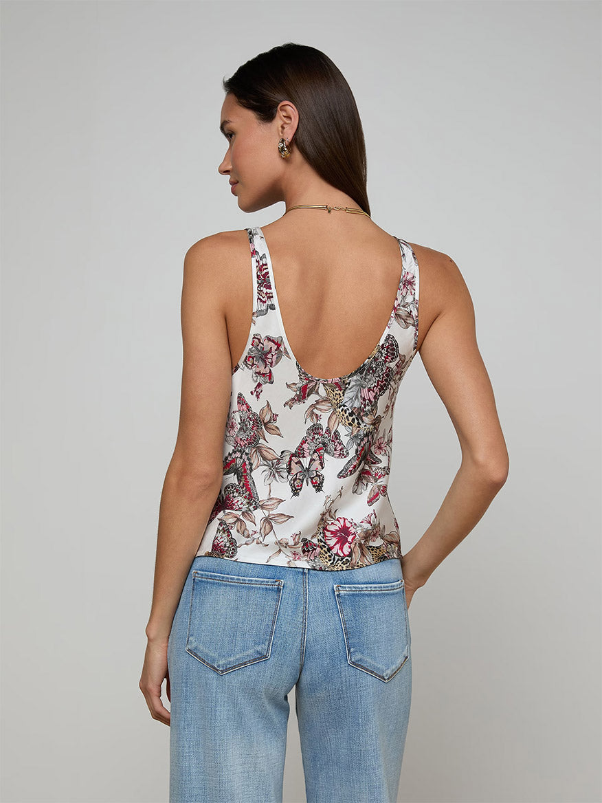 A woman is seen from behind wearing the L'Agence Eddie Tank in White Multi Small Butterfly Jungle and light blue jeans, set against a plain light gray background.