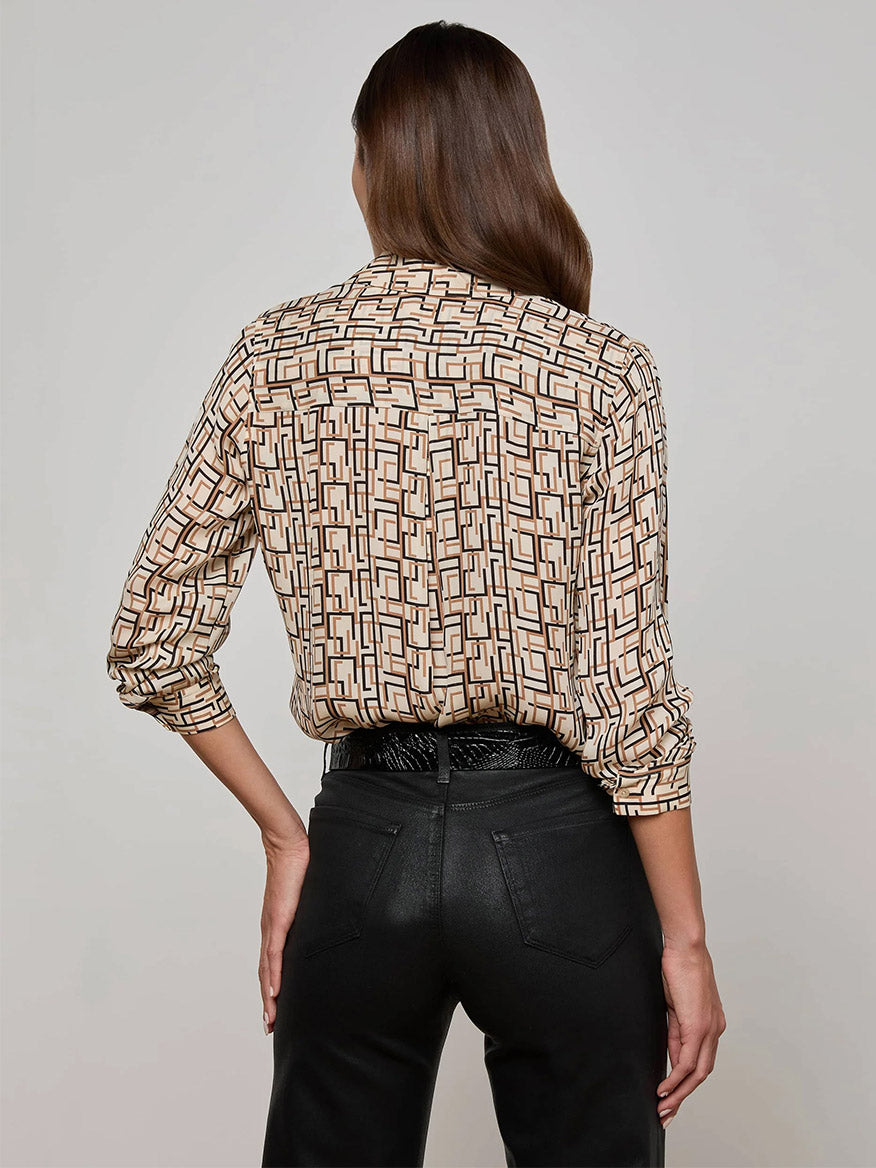 Person standing with their back to the camera, wearing the L'Agence Nina Silk Blouse in Ecru Multi Geo Print and black pants, right hand on hip.